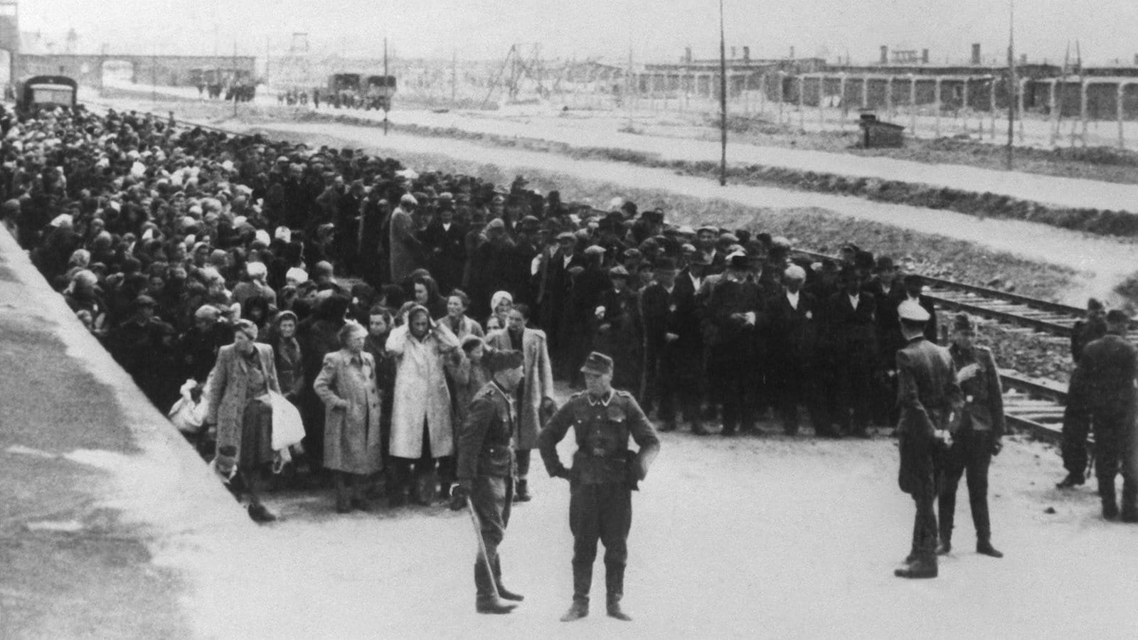 Neu angekommene Häftlinge haben auf der Todesrampe im KZ Auschwitz Aufstellung genommen. Links Frauen und Kinder, rechts die Männer. Im Hintergrund sind Gleisanlagen und Gebäude hinter Stacheldraht zu sehen. © Bildquelle dpa
